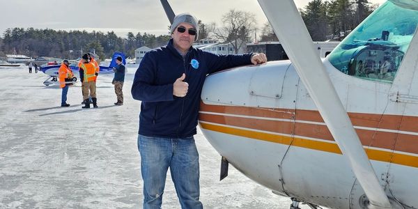 Man giving thumbs up beside a small airplane on a snowy runway.