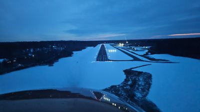 Airplane approaching a runway during dusk with snow-covered surroundings.