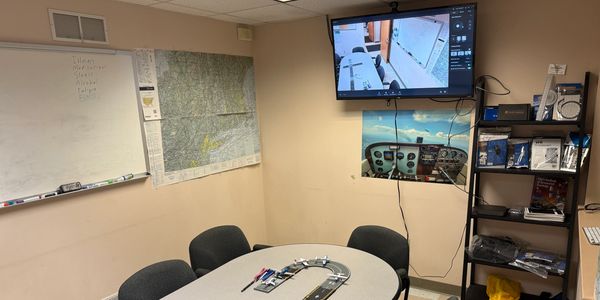 A small conference room with a table, chairs, and a monitor displaying a security camera feed.