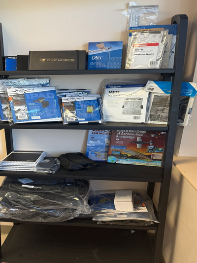 Shelves stocked with pilot logbooks, aviation handbooks, and flight training materials.