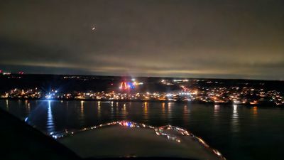 Nighttime aerial view of a city with illuminated buildings and reflections on water.