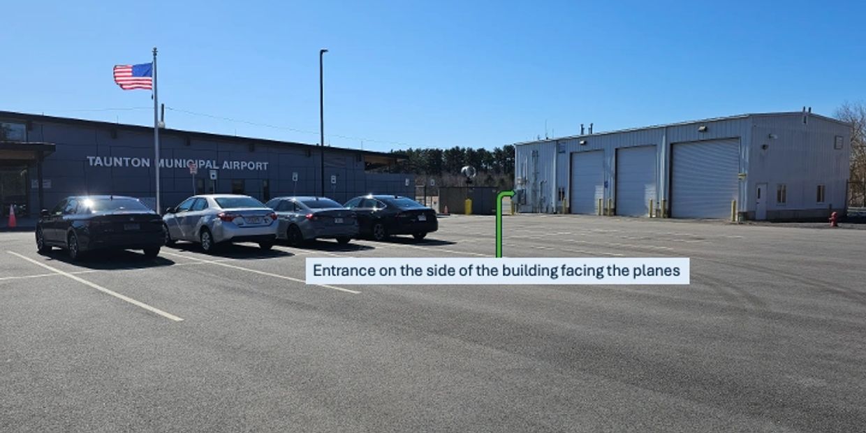 Parking lot outside Taunton Municipal Airport with cars and an entrance sign.